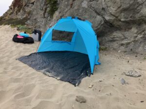 A blue tent is on the beach near some rocks.