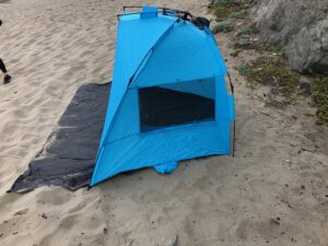 A blue tent is on the beach near some sand.