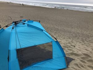 A blue tent on the beach near the ocean.