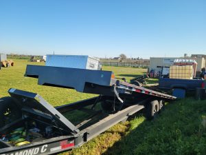 A 2021 Diamond Flat Bed 24' Trailer with tilt and winch on a grassy field.