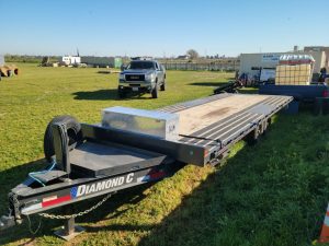 A 2021 Diamond Flat Bed 24' Trailer w/tilt and winch parked in a field.