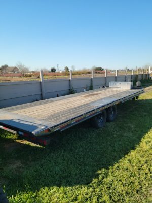 A 2021 Diamond Flat Bed 24' Trailer w/tilt and winch parked in a grassy area.
