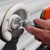 A person is putting a Add Fresh Water Tank Fill $25 Flat Fee plug into a white rv.