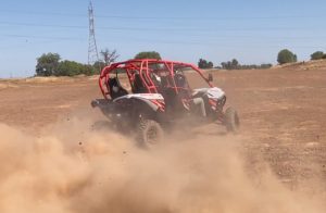 A man driving a 2017 Maverick Can-Am 4 person through a dirt field.