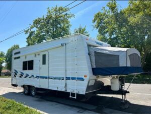 A white trailer with blue awning parked on the side of road.