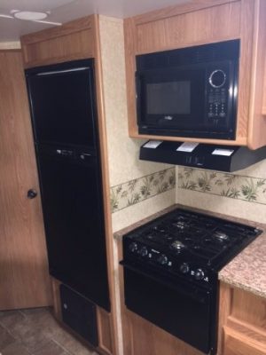 A kitchen in a small 2011 Rainier Dutchman Bunk House 28' with a stove and microwave.