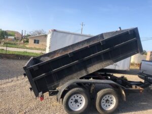 A dump trailer with the back open on gravel.