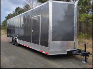 A black trailer with a silver trim parked on the side of a road.