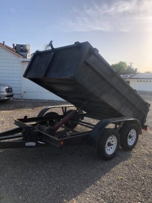 A dump trailer is parked in the dirt.