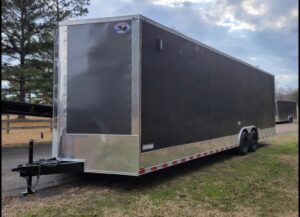 A large trailer parked in the grass near some trees.