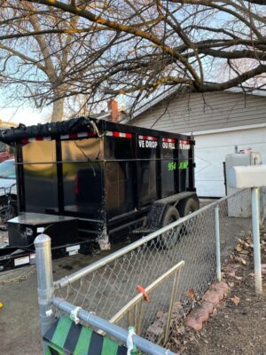 A black trailer with a large dumpster behind it.