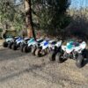 A row of four wheeler 's parked in the dirt.