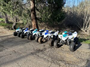 A row of four wheeler 's parked in the dirt.