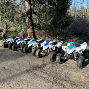 A row of four wheeler 's parked in the dirt.